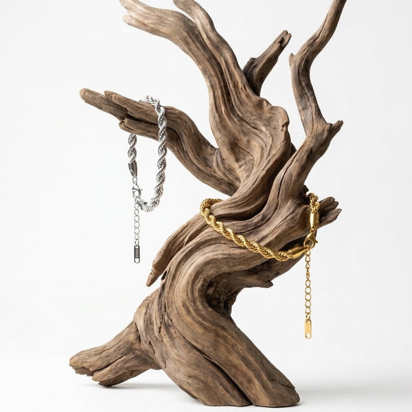 Aureliss Kordelarmbänder in Gold und Silber aus Edelstahl, präsentiert auf einem dekorativen Treibholz-Ständer.