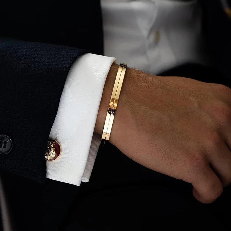 Aureliss Ryder Manschettenarmband aus goldfarbenem Edelstahl am Handgelenk eines Mannes im Anzug